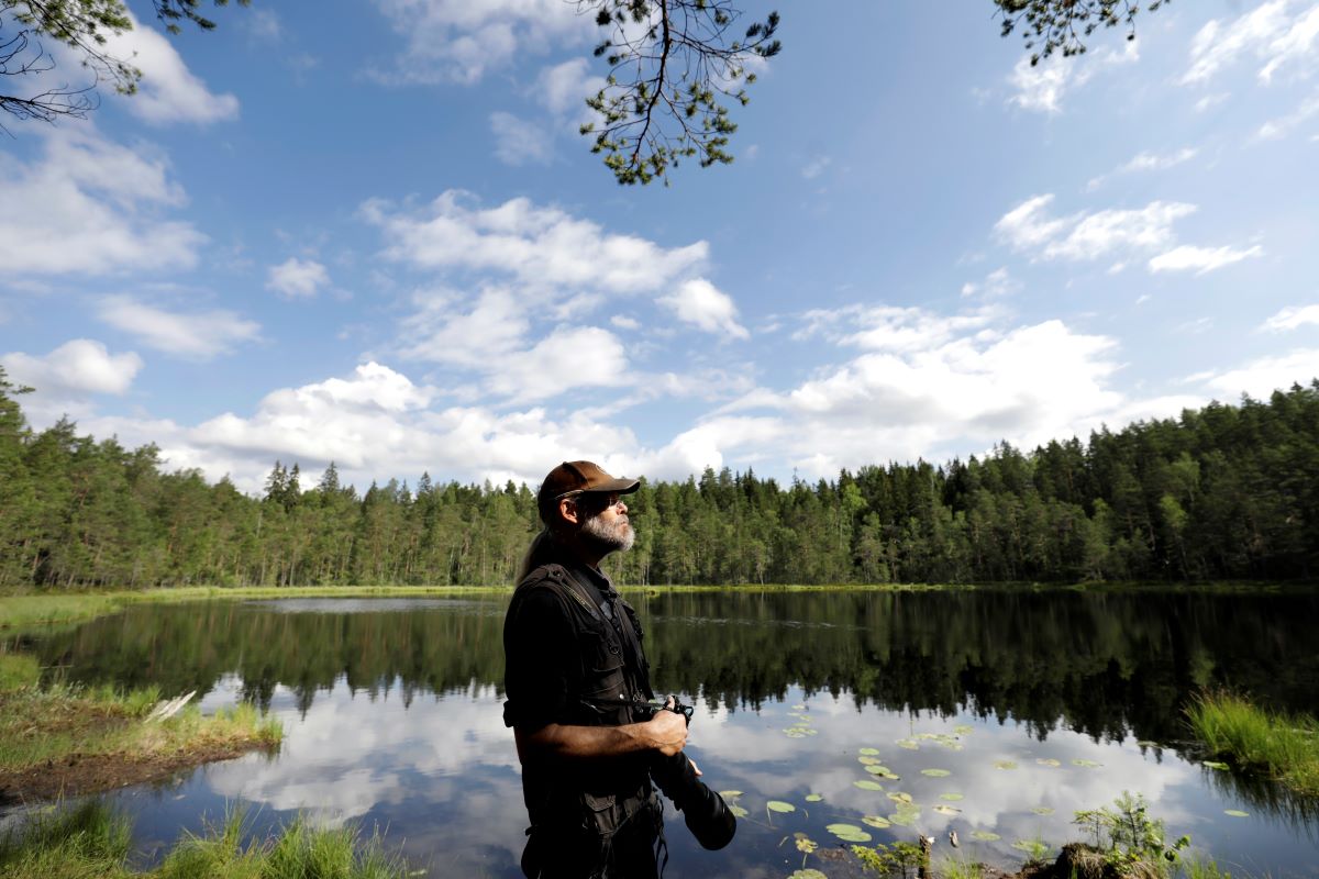 Haastateltava Markus Hotakainen kuvattuna metsälammen rannassa kamera kädessä.